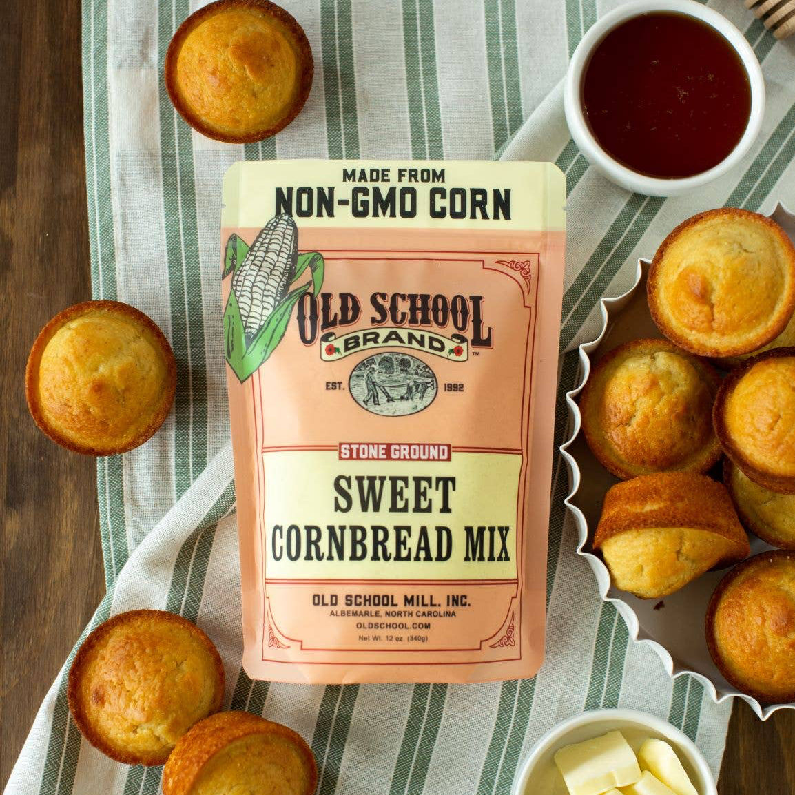 Packaging of Sweet Cornbread Mix by Old School Brand, with prepared cornbread muffins alongside butter and honey.