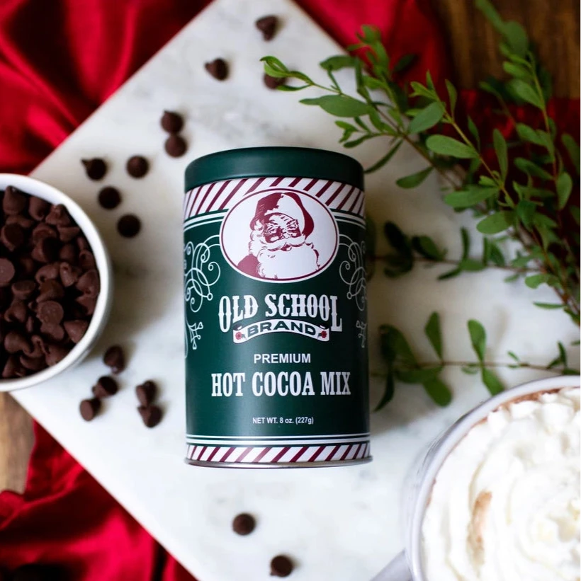 Old School Hot Cocoa Mix can with a mug of hot chocolate and chocolate chips on a red fabric background.