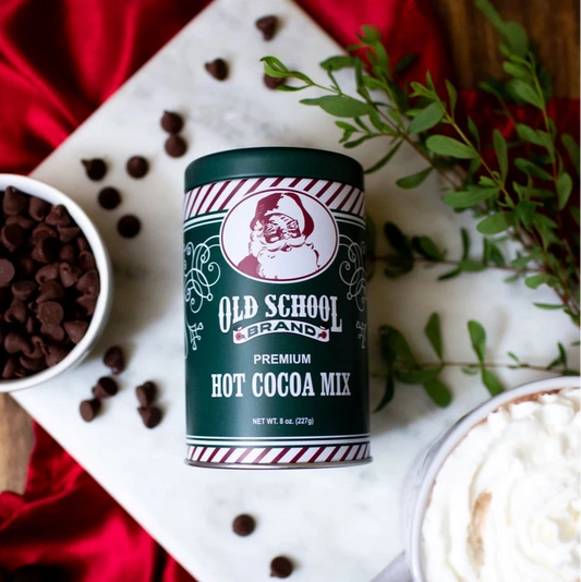 Old School Hot Cocoa Mix can with a mug of hot chocolate and chocolate chips on a red fabric background.